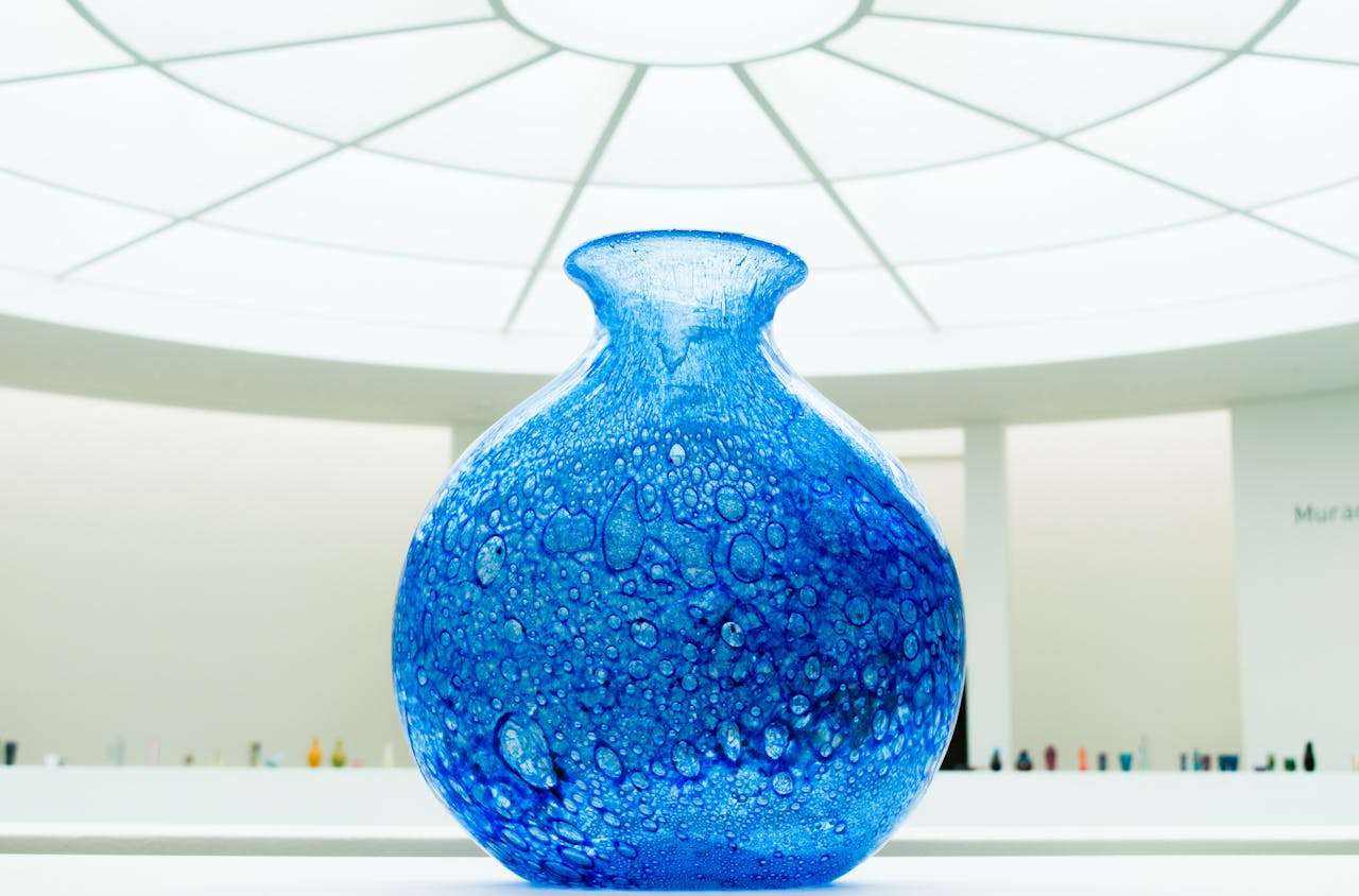 A stunning blue glass vase showcased in a contemporary museum setting with bright lighting.